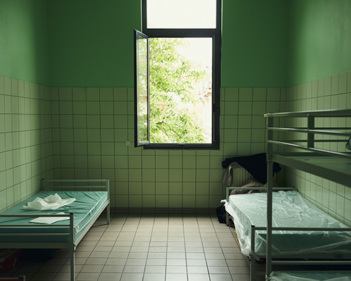 Chambre de centre d'hébergement avec 3 lits, fenêtre ouverte. Peinture des murs verte.